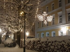 Una calle nevada con un árbol decorado con luces de adorno y un edificio con varias ventanas.