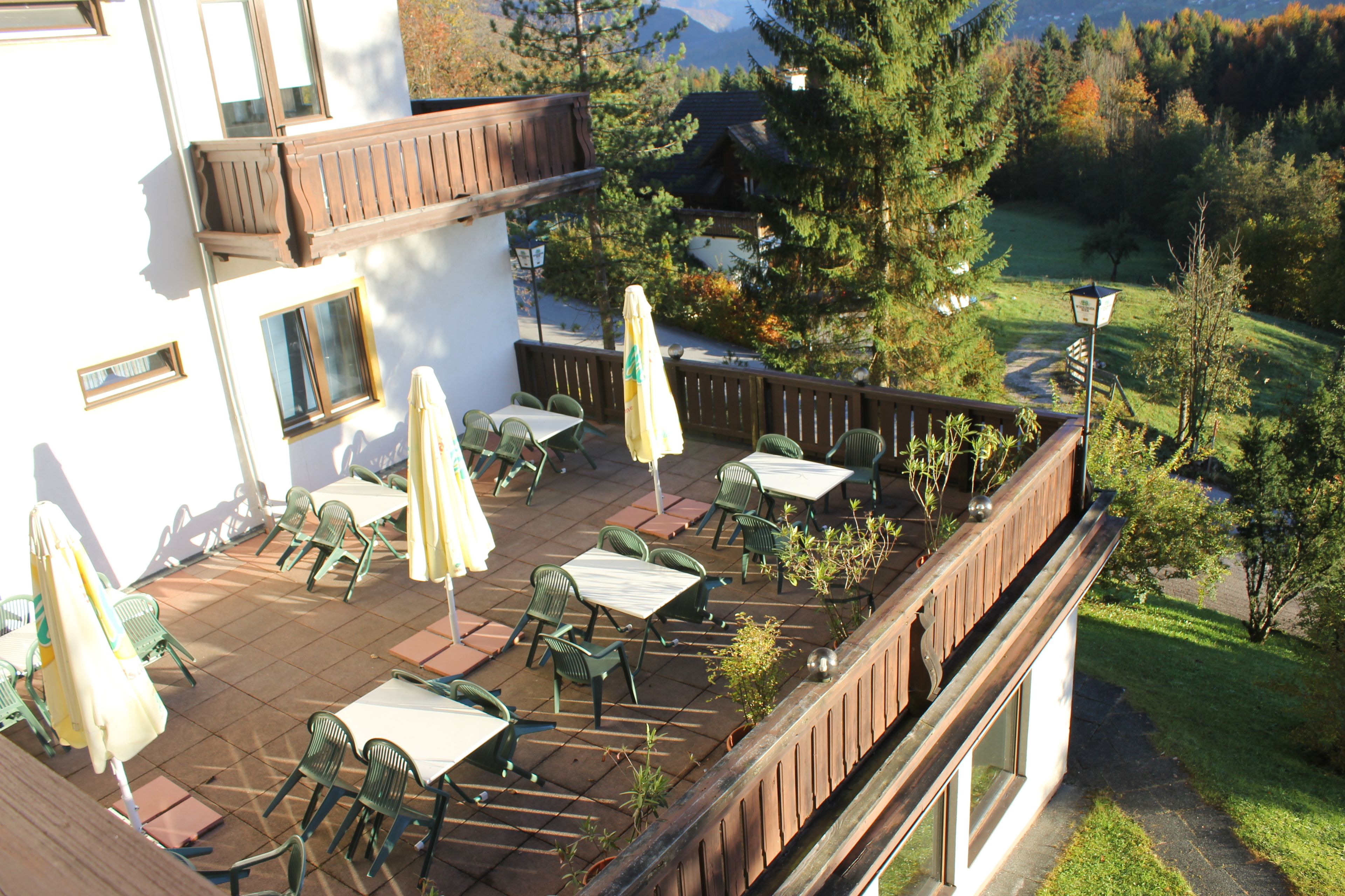A terrace with outdoor seating, a view of a forest, and a building with a balcony.