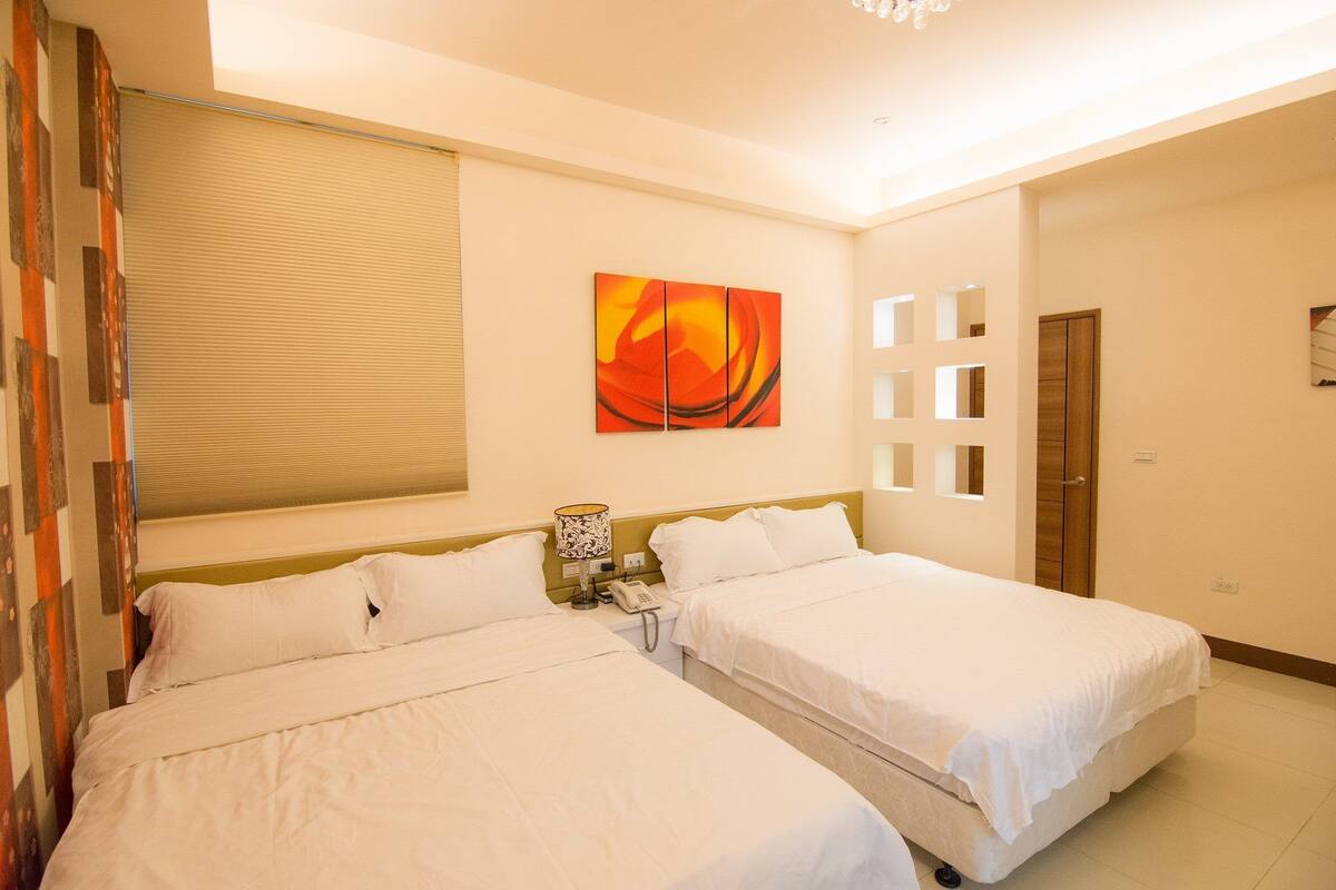 A hotel room with two beds, a painting on the wall, a telephone, and a door.