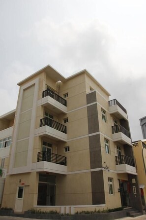 Un immeuble résidentiel à plusieurs étages, doté de balcons, d’un toit plat et d’une façade beige.