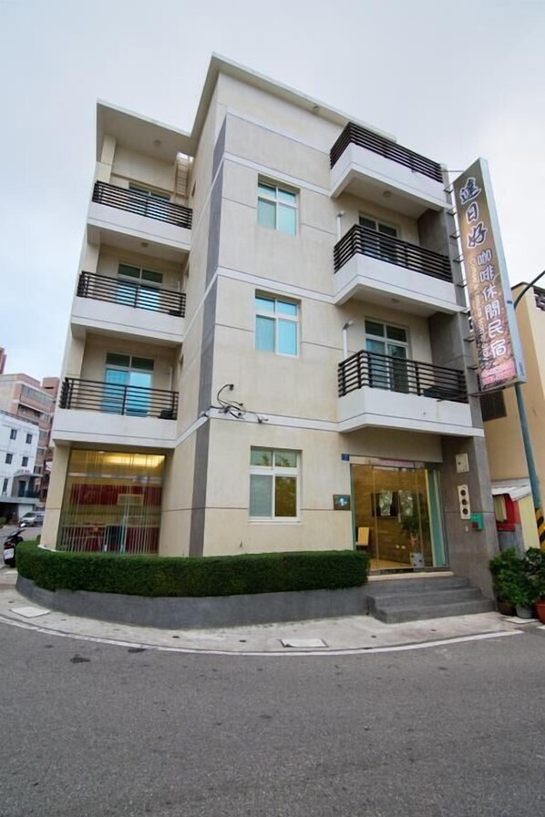 Un immeuble à plusieurs étages, doté d’une architecture moderne, avec des balcons à chaque niveau, une entrée bien visible et une enseigne avec du texte.