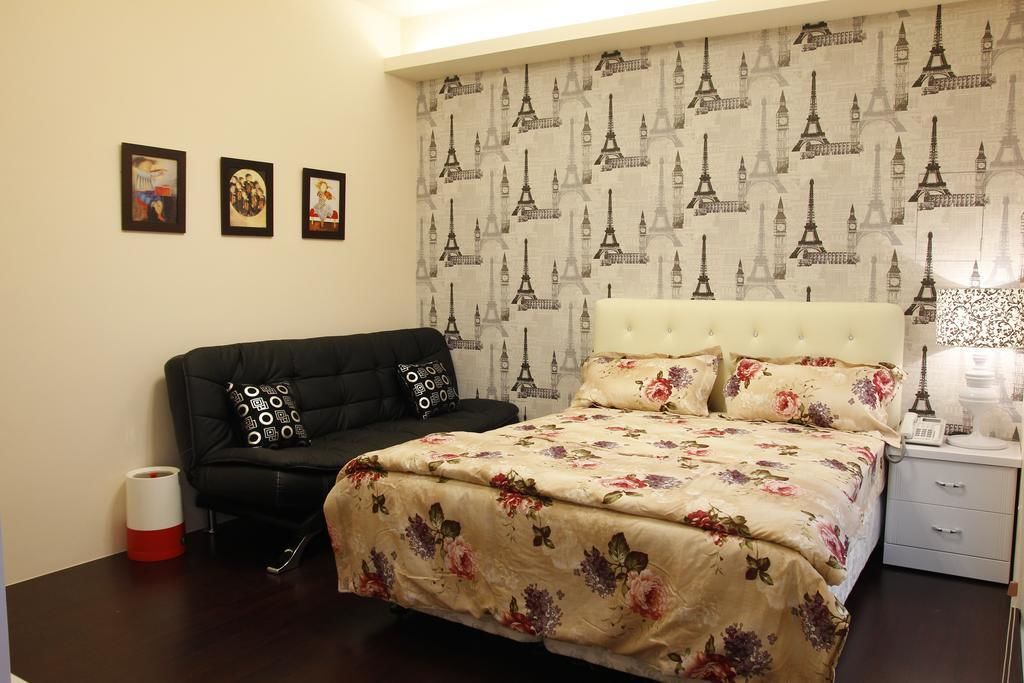 Un dormitorio con una cama, un sofá negro, una mesita de noche blanca y una pared decorada con un diseño de la Torre Eiffel.