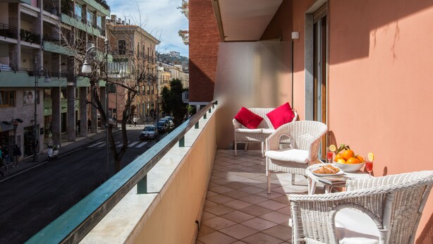 Een balkon met rieten meubilair, een tafel met fruit, en uitzicht op de straat.