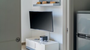 Een moderne woonkamer met een flatscreen televisie aan de muur, een witte kast eronder en een klein boekenrek.