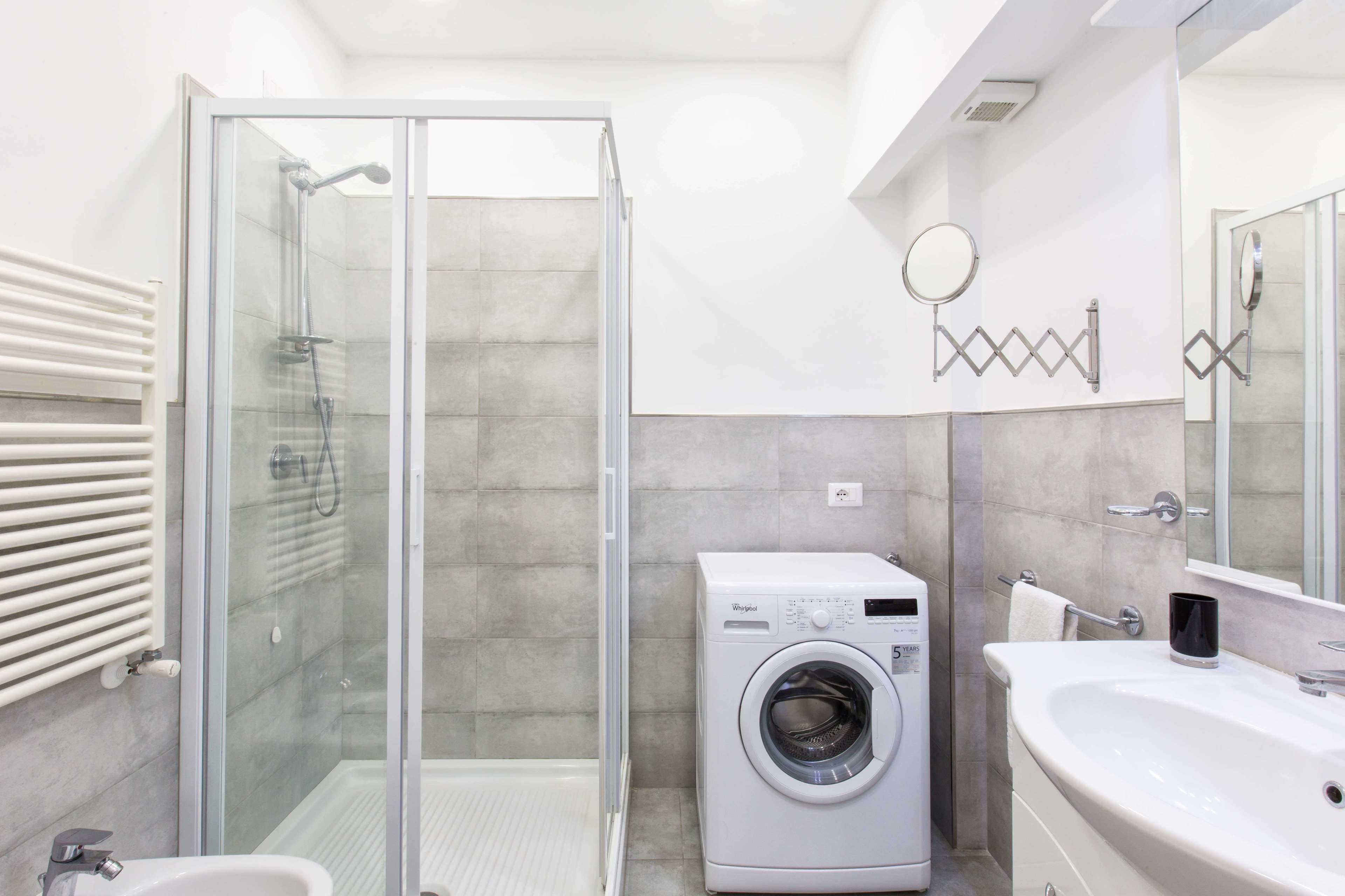 Une salle de bain moderne dotée d’une douche à parois de verre, d’un lave-linge encastré et d’un grand lavabo avec un miroir.
