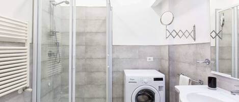 Une salle de bain moderne dotée d’une douche à parois de verre, d’un lave-linge encastré et d’un grand lavabo avec un miroir.