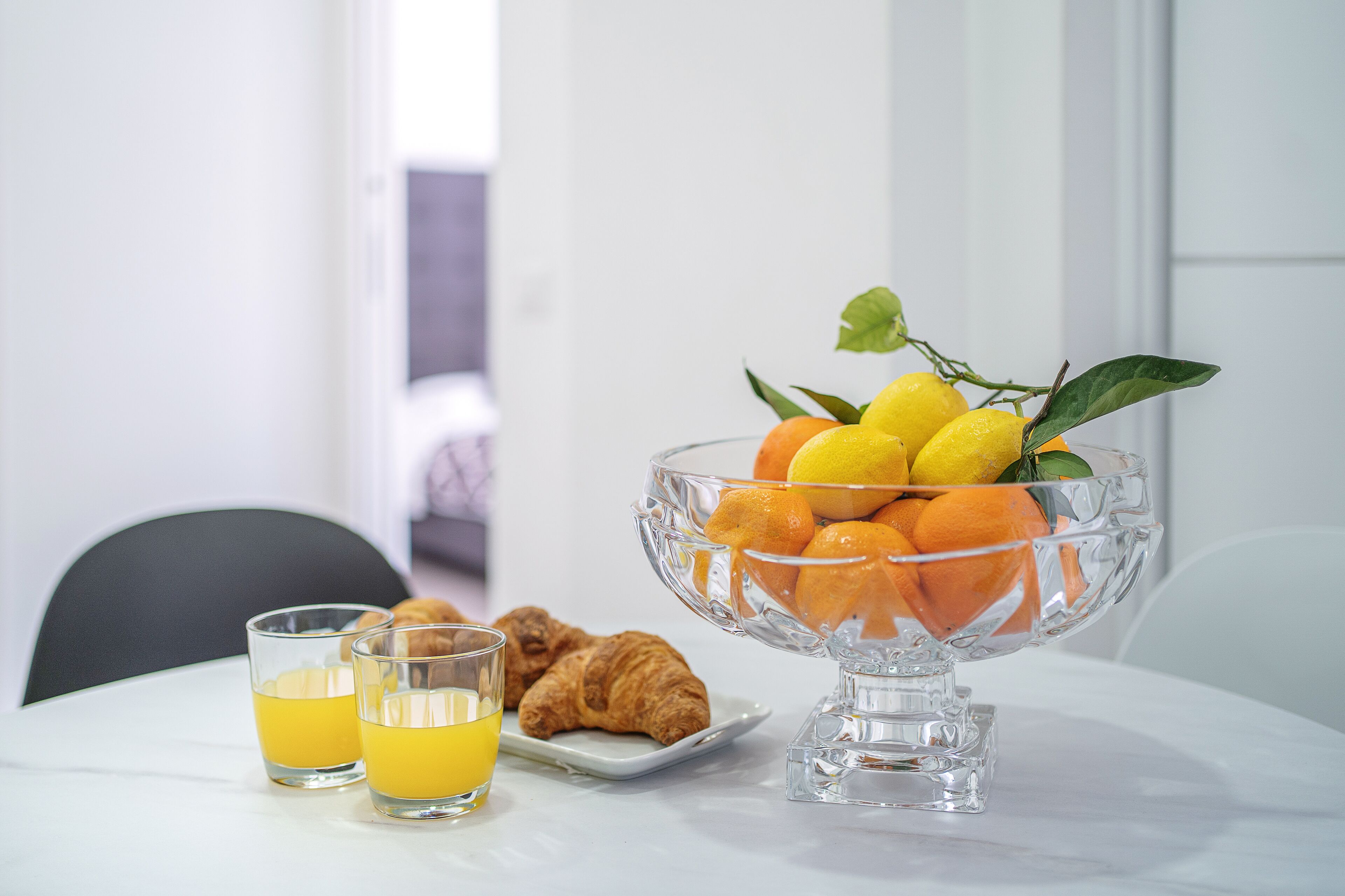A breakfast setting with a fruit bowl, croissants, and orange juice glasses on a table.
