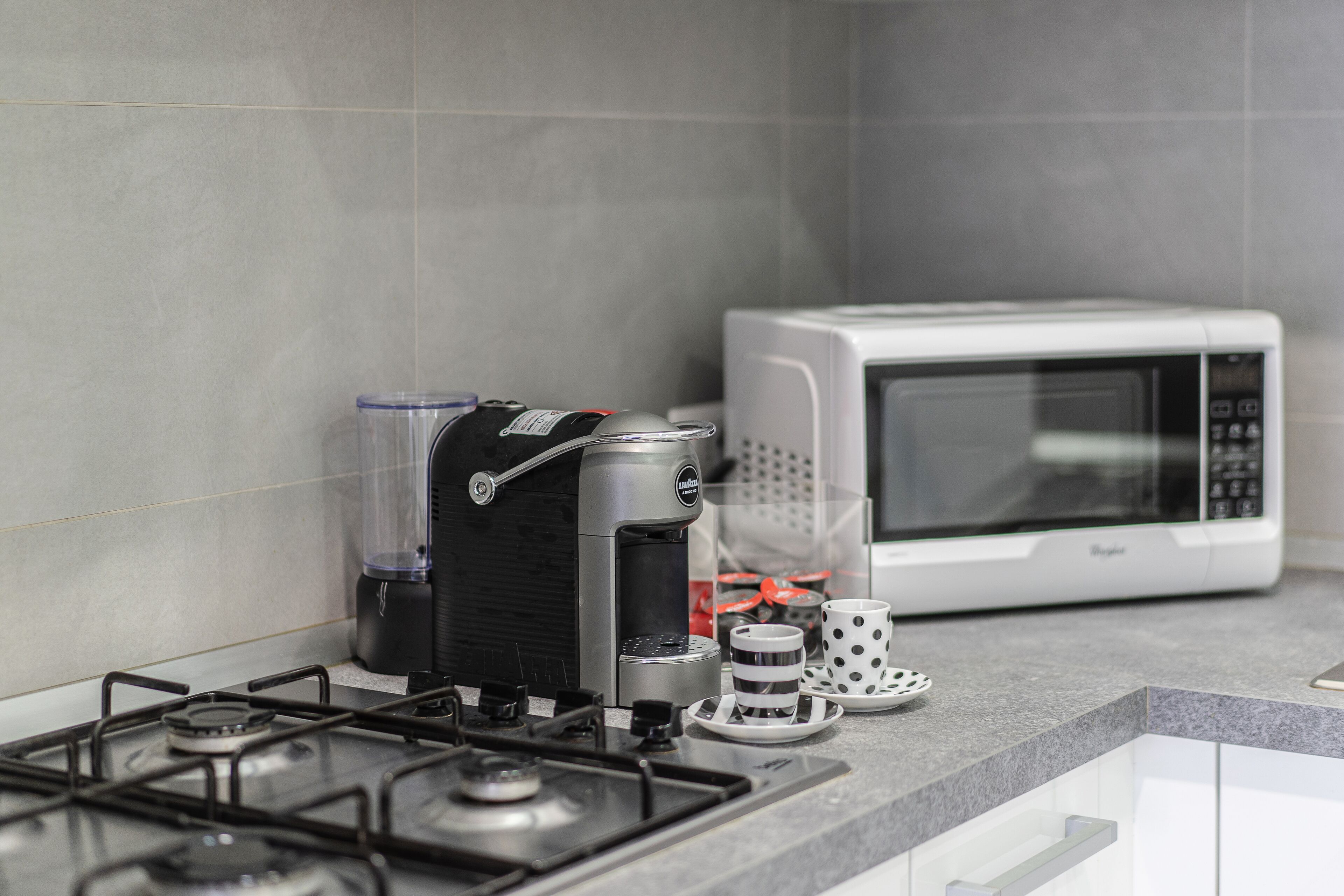 A kitchen with a gas stove, a coffee maker, a microwave, and a coffee cup on the counter.