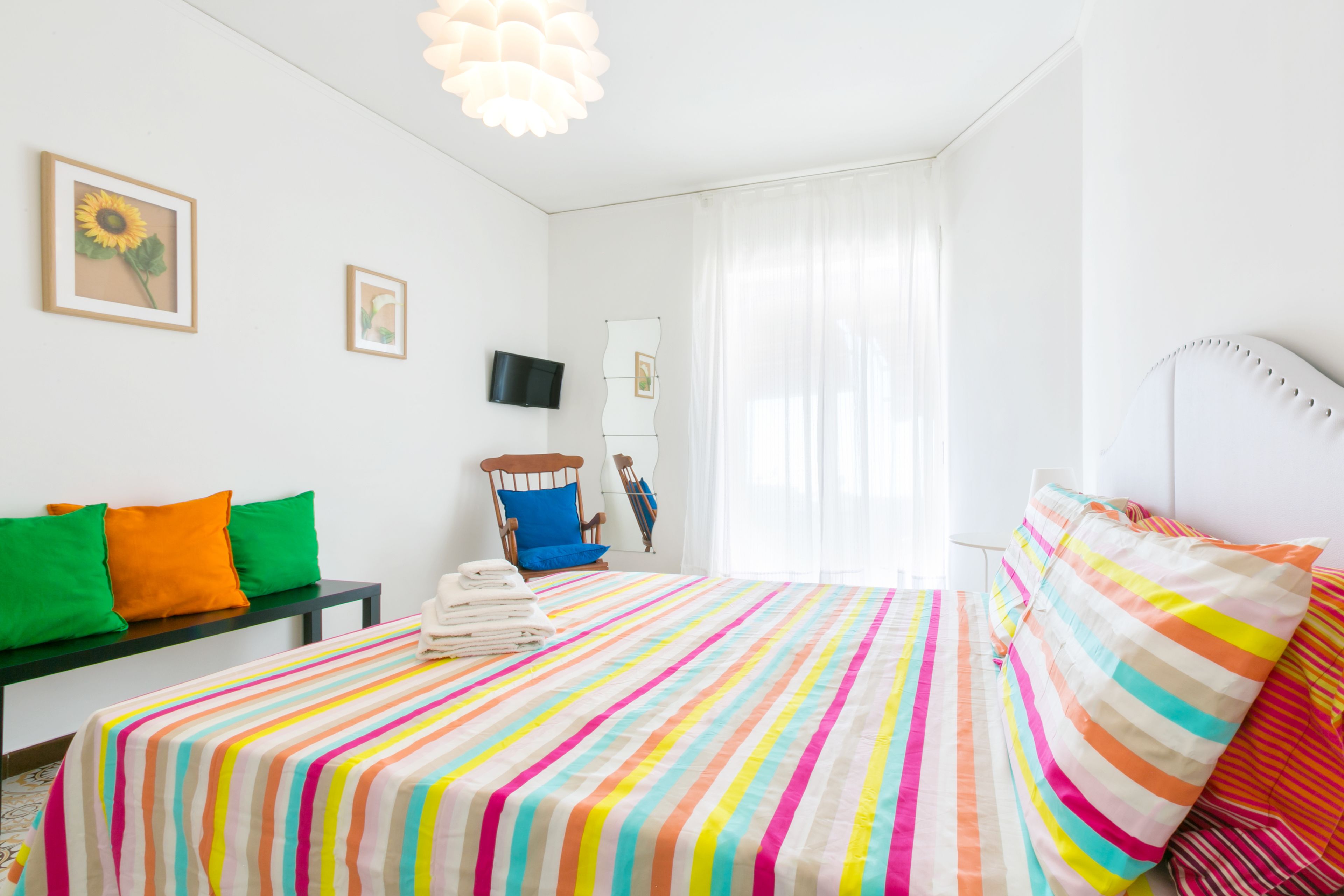Una habitación de hotel con una cama grande, un escritorio con silla, televisión y una ventana con cortinas traslúcidas.