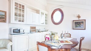 Un coin repas avec une table en bois, des meubles blancs et une fenêtre ronde.