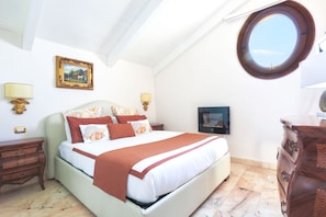 A bedroom with a bed, a dresser, a nightstand, a lamp, a framed picture, and a round mirror.