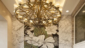 En entréhall med ett marmorgolv, en väggmålning med blommotiv, en kristallkrona och krukväxter.
