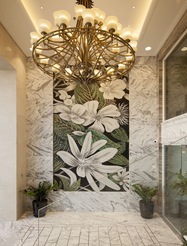 A lobby with a marble floor, a floral mural, a chandelier, and potted plants.