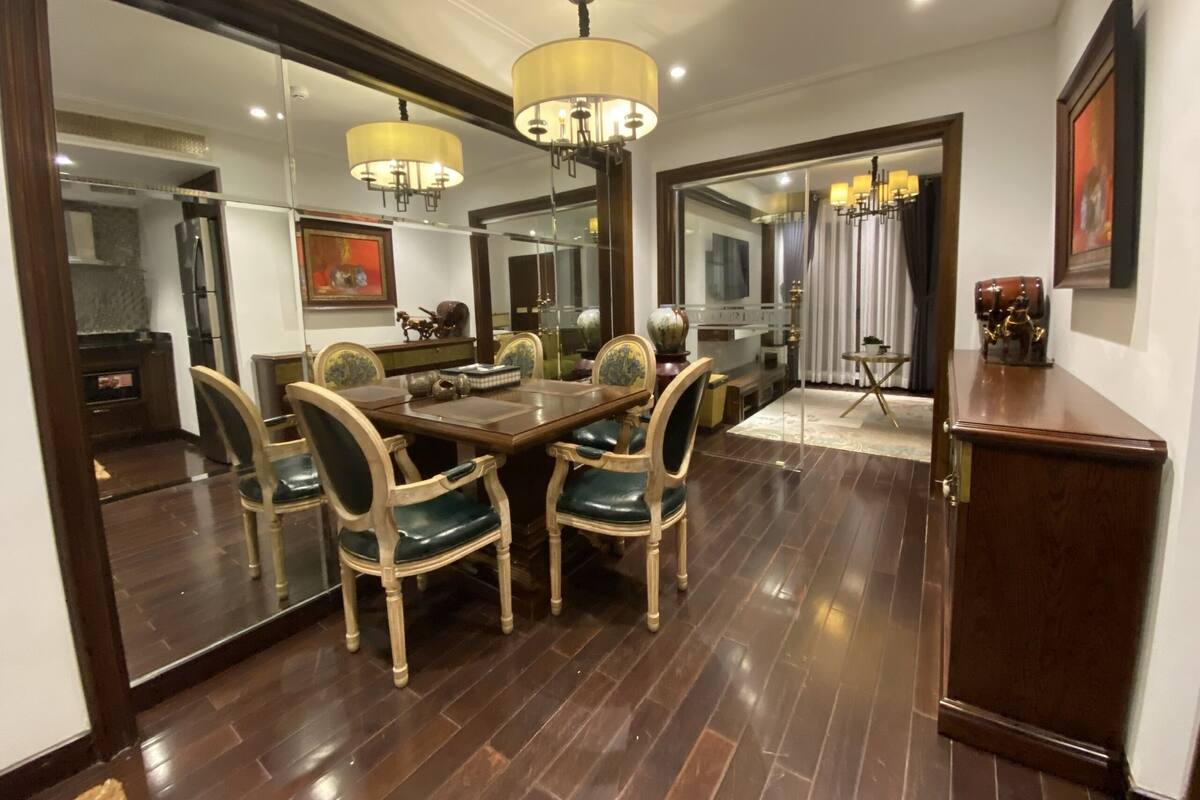 A dining area with a wooden table and chairs, a chandelier, and a large mirror reflecting the room.