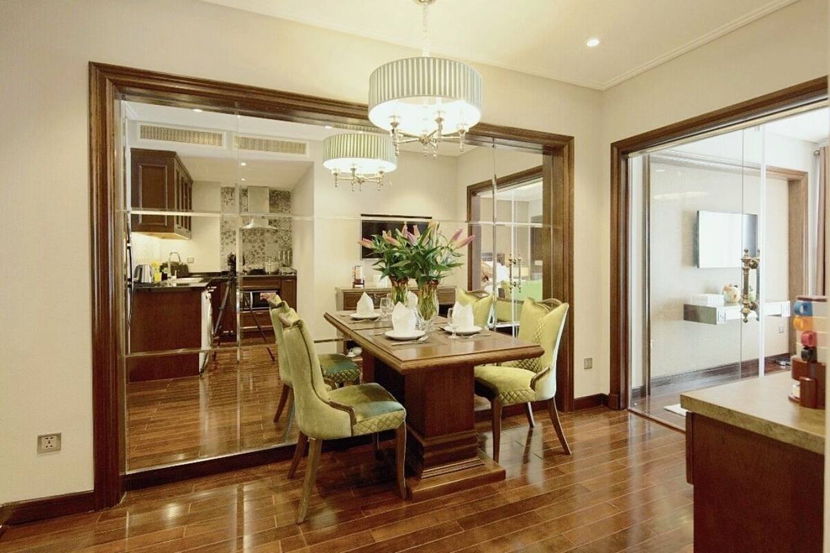 A spacious dining area with a wooden table and chairs, a chandelier, and a large mirror reflecting the kitchen.