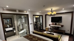 Ett hotellrum med en stor säng, en TV, en soffa, en duschkabin med glasväggar och en matplats.