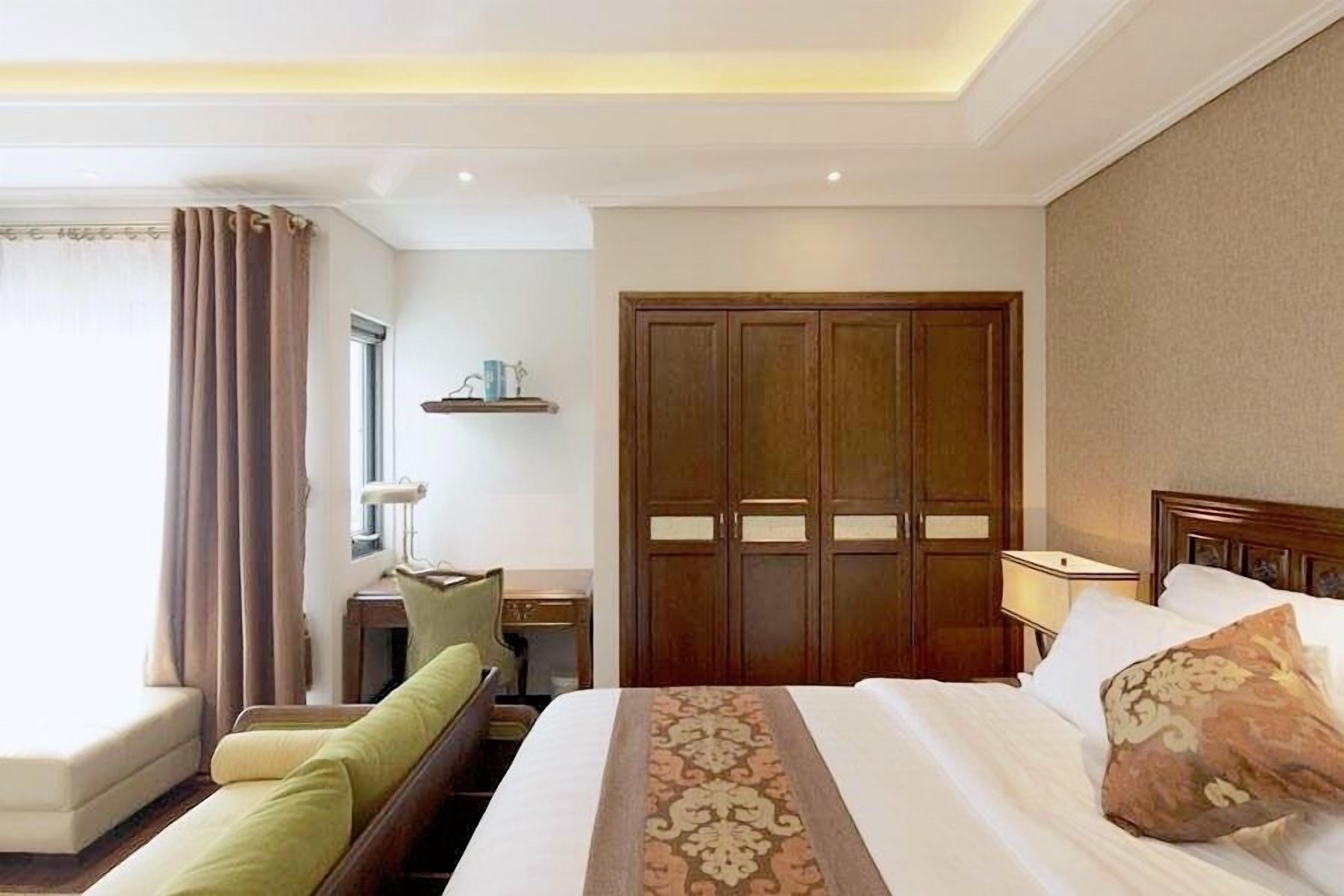 A hotel room with a bed, a desk, a chair, a wardrobe, and a window with curtains.