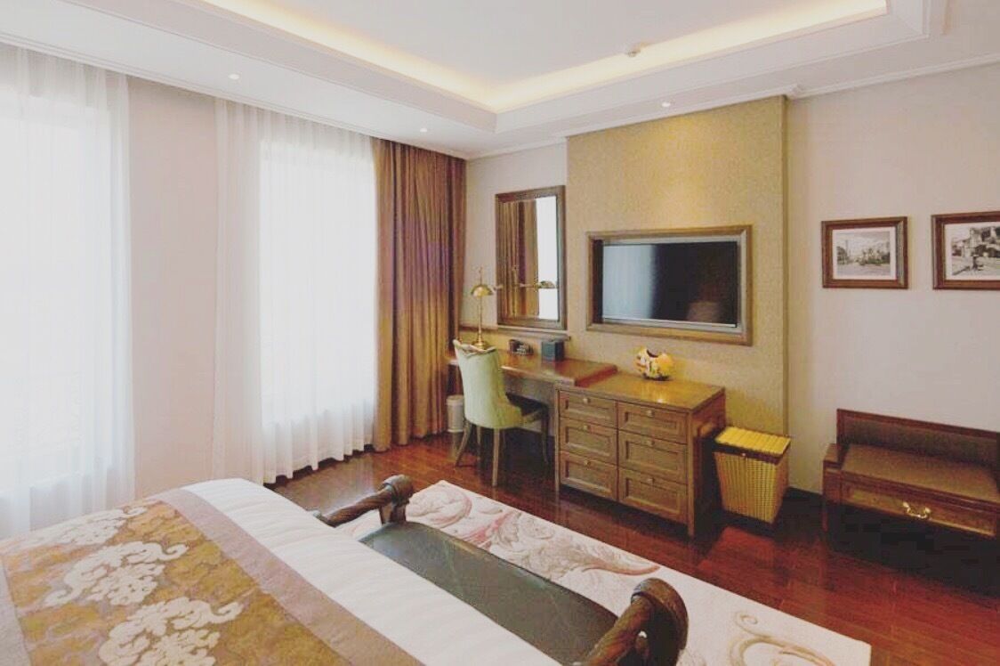 A hotel room with a bed, a desk, a chair, a television, and a dresser.
