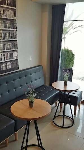 A modern lounge area with a dark blue sofa, two round wooden tables with black metal legs, and a bookshelf filled with books. - Avra Hotel (Katerini)
