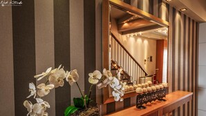 A modern interior with a wooden console table, white orchids, a mirror, and striped wallpaper. - Avra Hotel (Katerini)