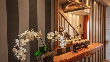 A modern interior with a wooden console table, white orchids, a mirror, and striped wallpaper.