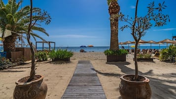 A wooden pathway leading to a beach with palm trees and beach umbrellas.