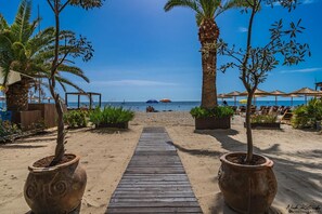 A wooden pathway leading to a beach with palm trees and beach umbrellas. - Avra Hotel (Katerini)