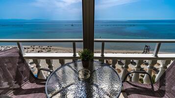 Un balcón con una mesa de vidrio, sillas y una planta en maceta. Se ve una playa y el mar.