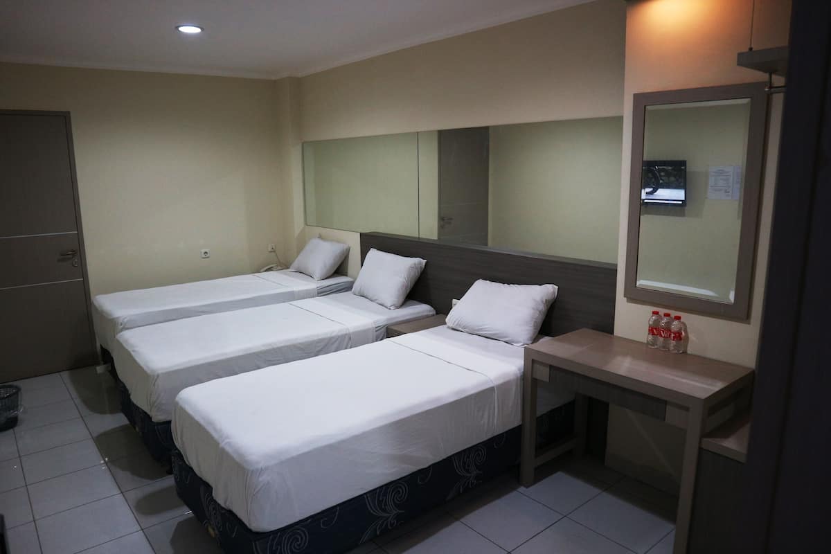Una habitación de hotel con tres camas individuales, un escritorio pequeño, un espejo y una puerta.