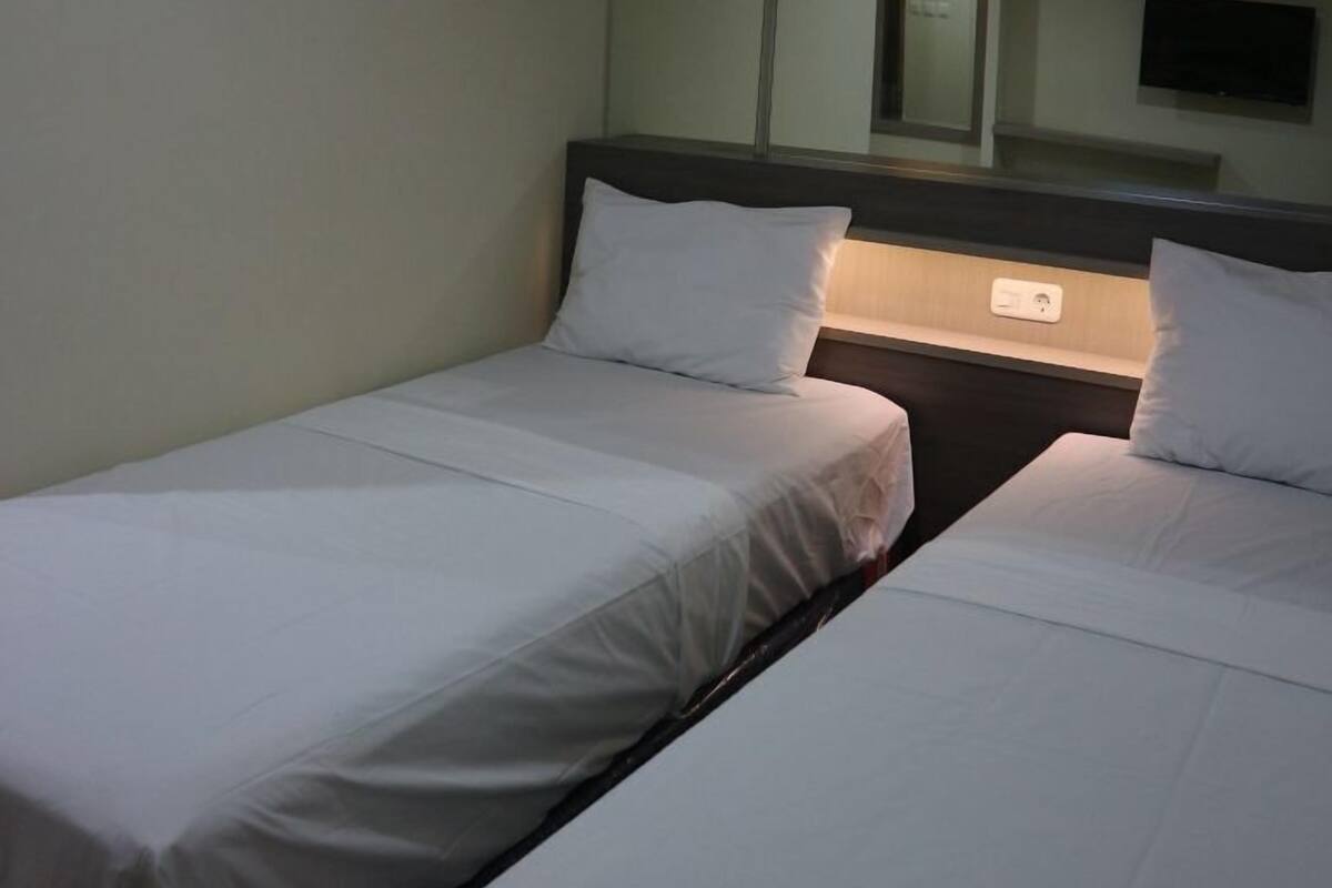 Una habitación de hotel con dos camas individuales, una mesita de noche, un espejo y un televisor.