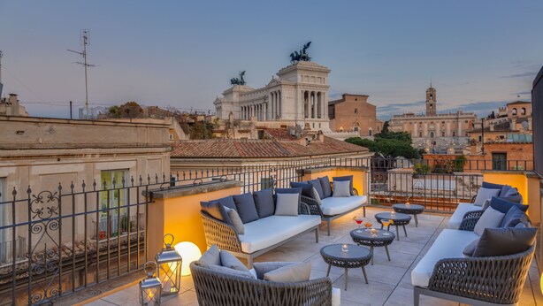 A rooftop terrace with outdoor seating, a view of historical buildings, and a statue. - Otivm Hotel (Rome)