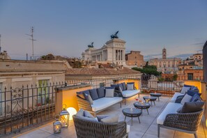 A rooftop terrace with outdoor seating, a view of historical buildings, and a statue. - Otivm Hotel (Rome)