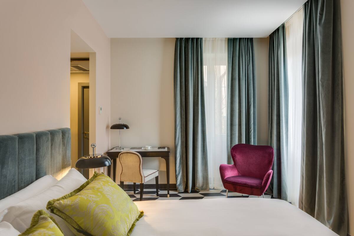 A hotel room with a bed, a desk, a chair, and a window with curtains.