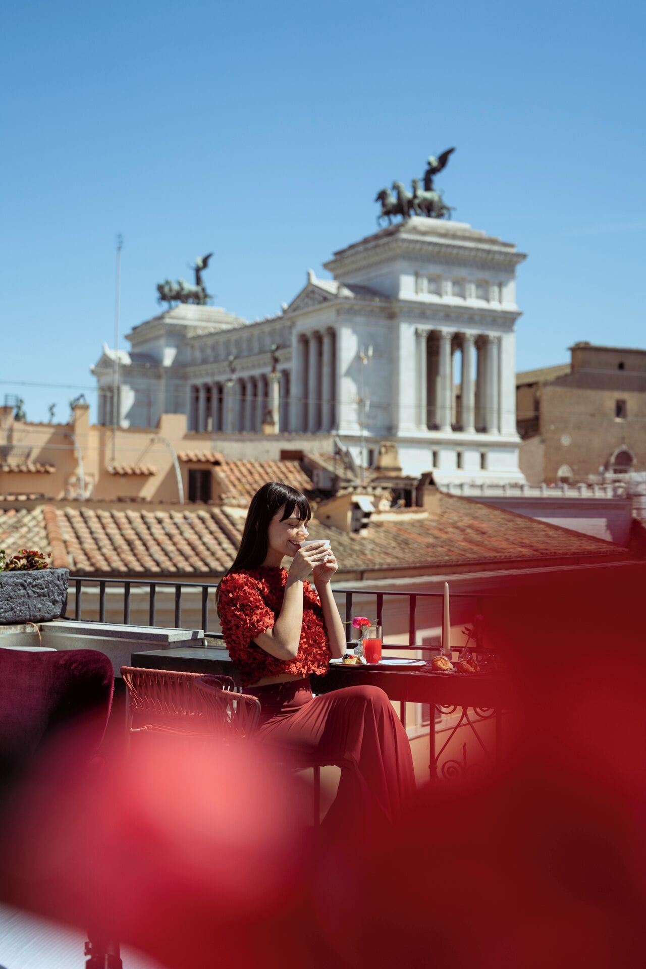 A person sitting on a balcony with a view of a classical building with columns and statues.