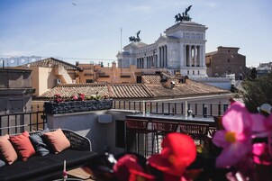 Una terraza en la azotea con vistas a un edificio de estilo clásico, un sofá exterior negro y un arreglo floral.