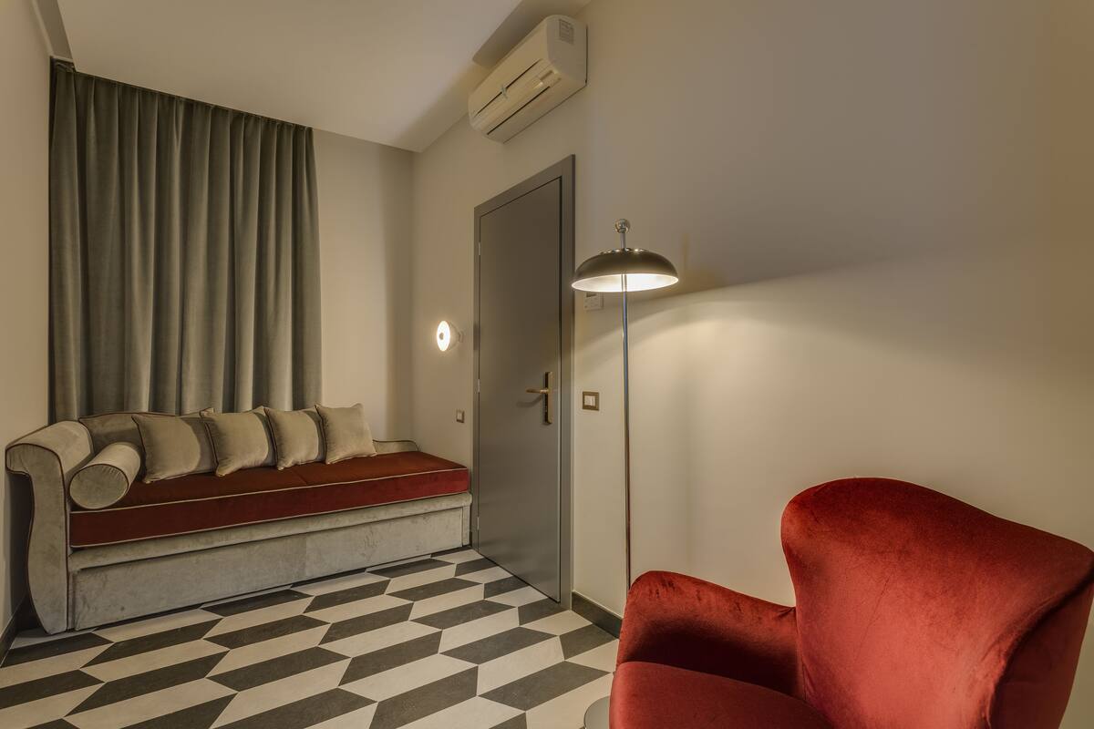 A room with a sofa, a red chair, a patterned floor, a door, and a lamp.