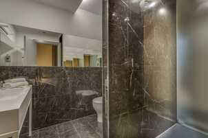 A modern bathroom with a marble vanity, a toilet, and a glass-enclosed shower area.