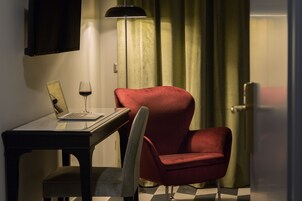 A room with a desk, a red chair, a laptop, a wine glass, a floor lamp, and a curtain.