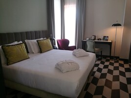 A hotel room with a large bed, a desk, a chair, and a lamp.