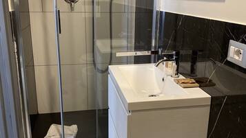 Een moderne badkamer met een douchecabine van glas, een wit wastafelmeubel en een zwart marmeren spatwand.