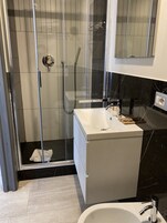 A modern bathroom with a glass-enclosed shower, a white vanity, and a black marble backsplash.