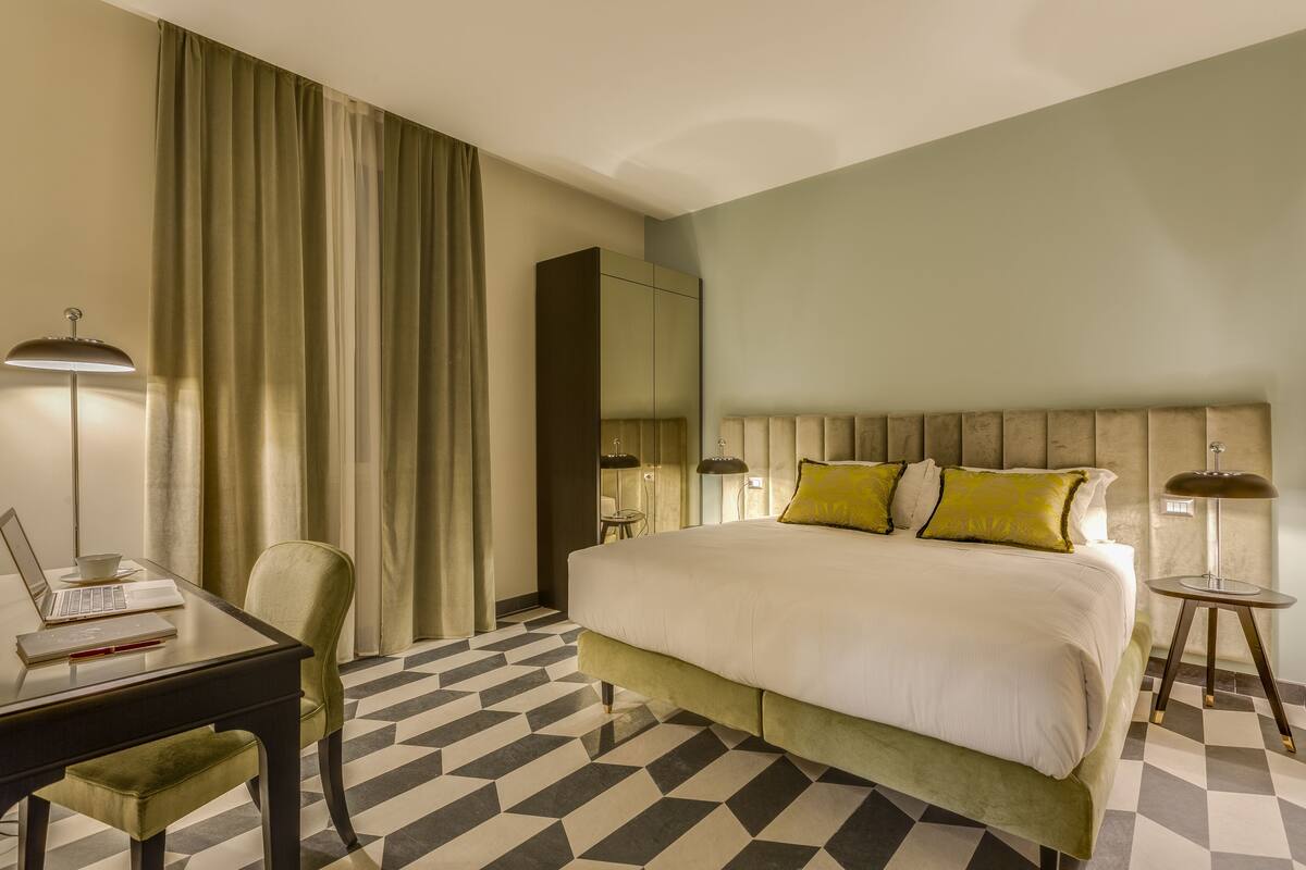 A hotel room with a large bed, a desk with a laptop, a chair, and a lamp.