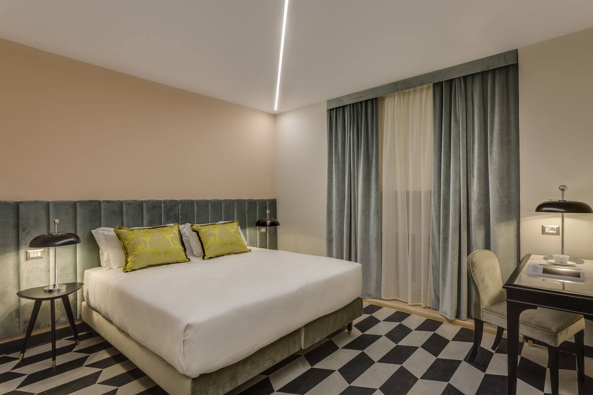 A hotel room with a bed, a desk, a chair, and a large window with curtains.