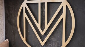 A logo on a dark textured wall, with a brown sofa and cushions in the foreground. - Otivm Hotel (Rome)