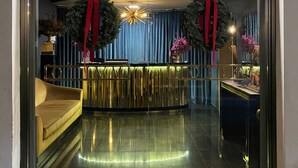 A hotel entrance with a sign reading "OTIVM". Inside, there is a reception desk with a gold finish, a blue curtain backdrop, and a chandelier. - Otivm Hotel (Rome)