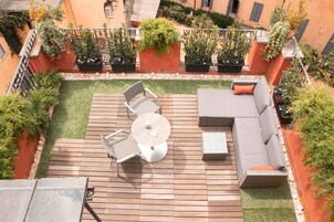 En tagterrasse med en træterrasse, et rundt bord, to stole, en sofa og krukker med planter.