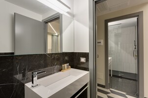 Een moderne badkamer met een witte wastafel, een zwart marmeren spatwand en een douchecabine van glas.