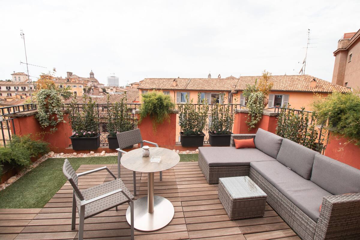 An outdoor patio with a round table, two chairs, a sofa, and potted plants.