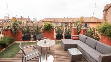 An outdoor patio with a round table, two chairs, a sofa, and potted plants.
