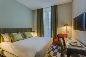 Habitación de hotel con cama, escritorio con silla, televisor y ventana con cortinas.